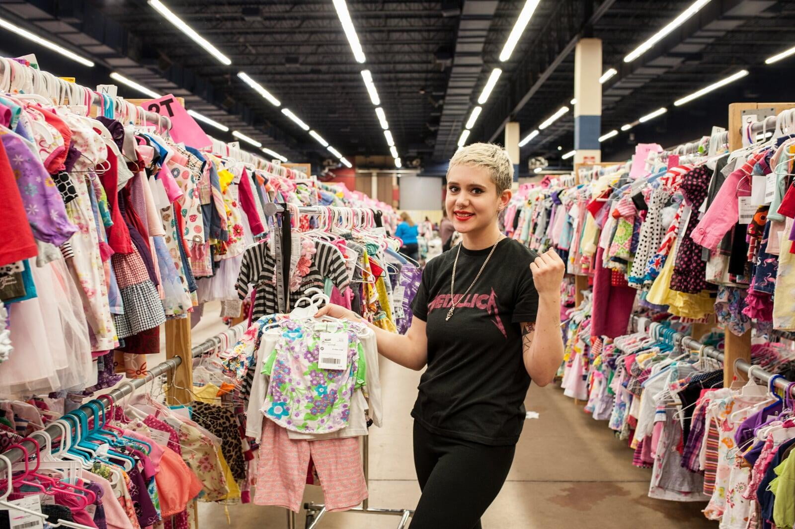 A JBF shopper mom in a black Metallica T-shirt holds an outfit she intends to buy at the JBF sale.